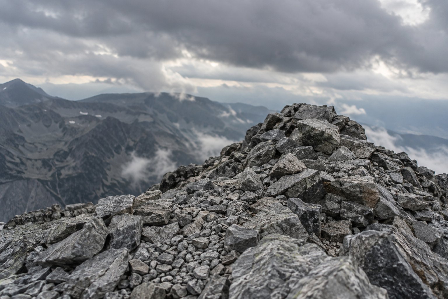 A bare mountain summit under heavy cloud, loose rock underfoot and no vegetation in sight