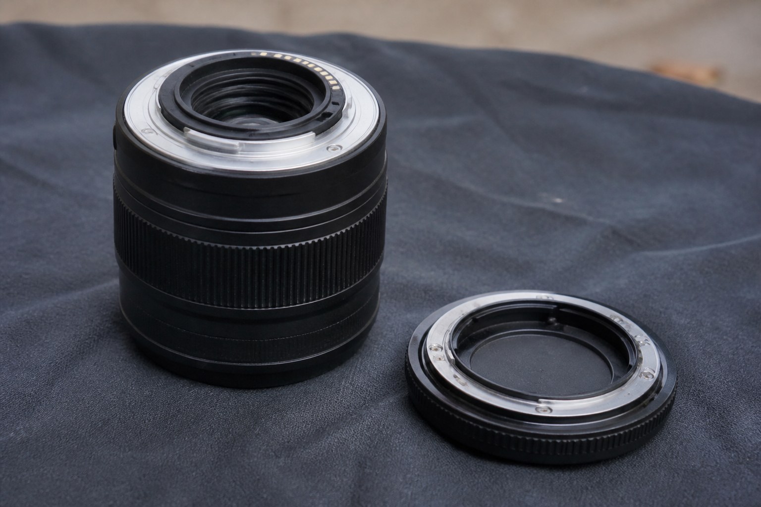 A camera lens beside its body cap on dark cloth, mount rings facing up