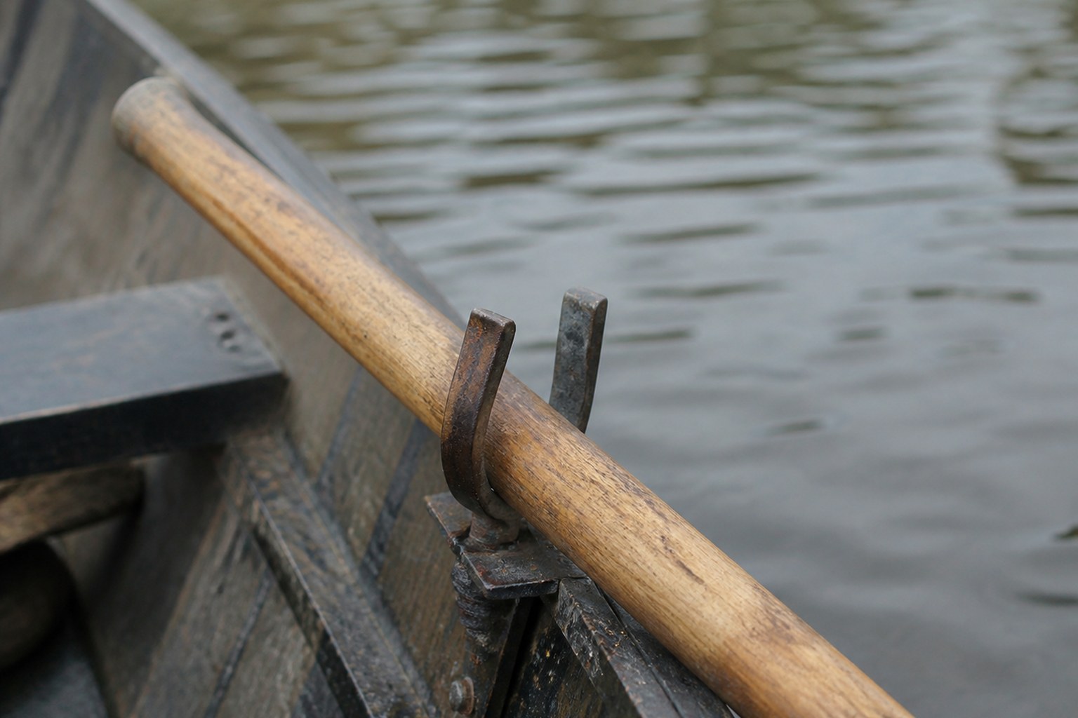 A wooden oar seated in the iron rowlock of a small boat
