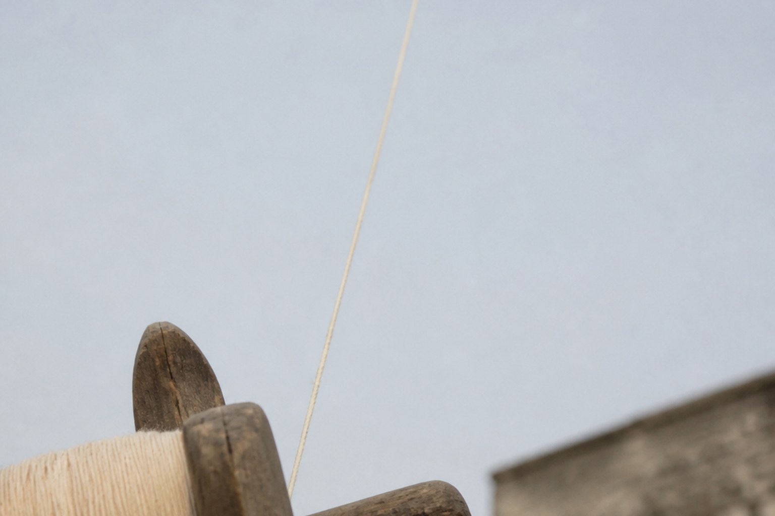 A kite line running from a wooden winder up out of frame against pale sky