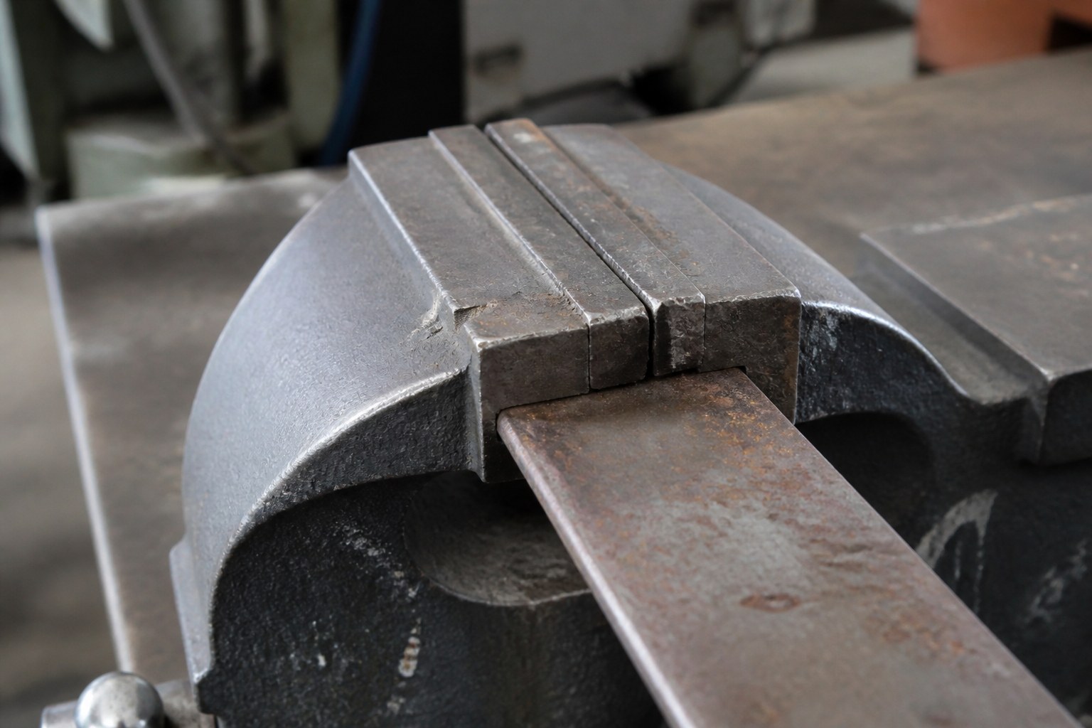 The jaws of a bench vice closed on a length of flat steel bar