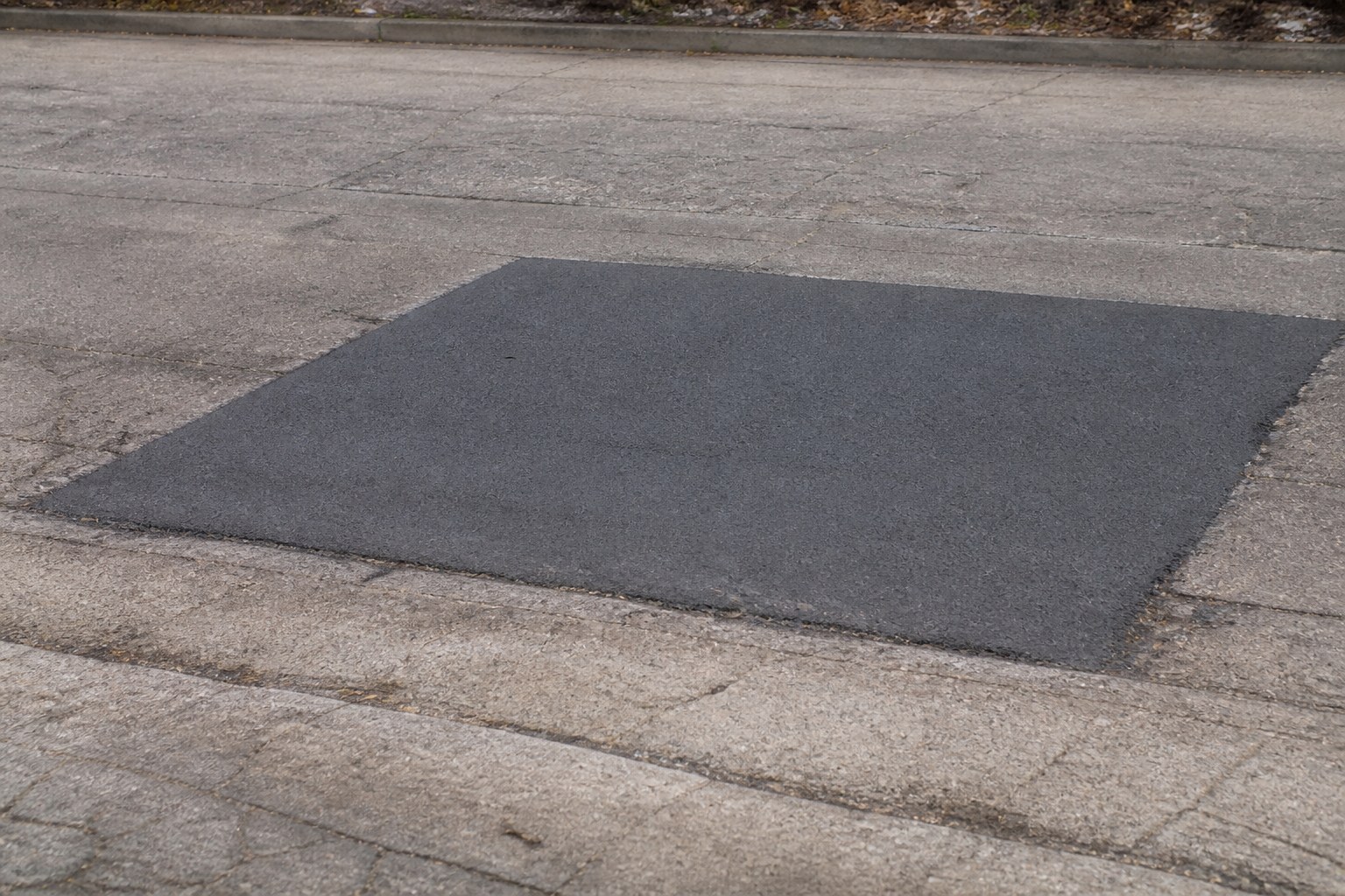 A rectangular asphalt patch set into an older road surface