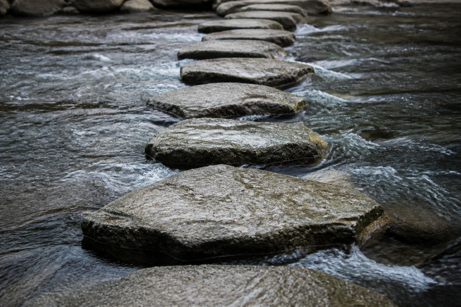 A line of flat stepping stones crossing a shallow river, water running fast in the gaps between them