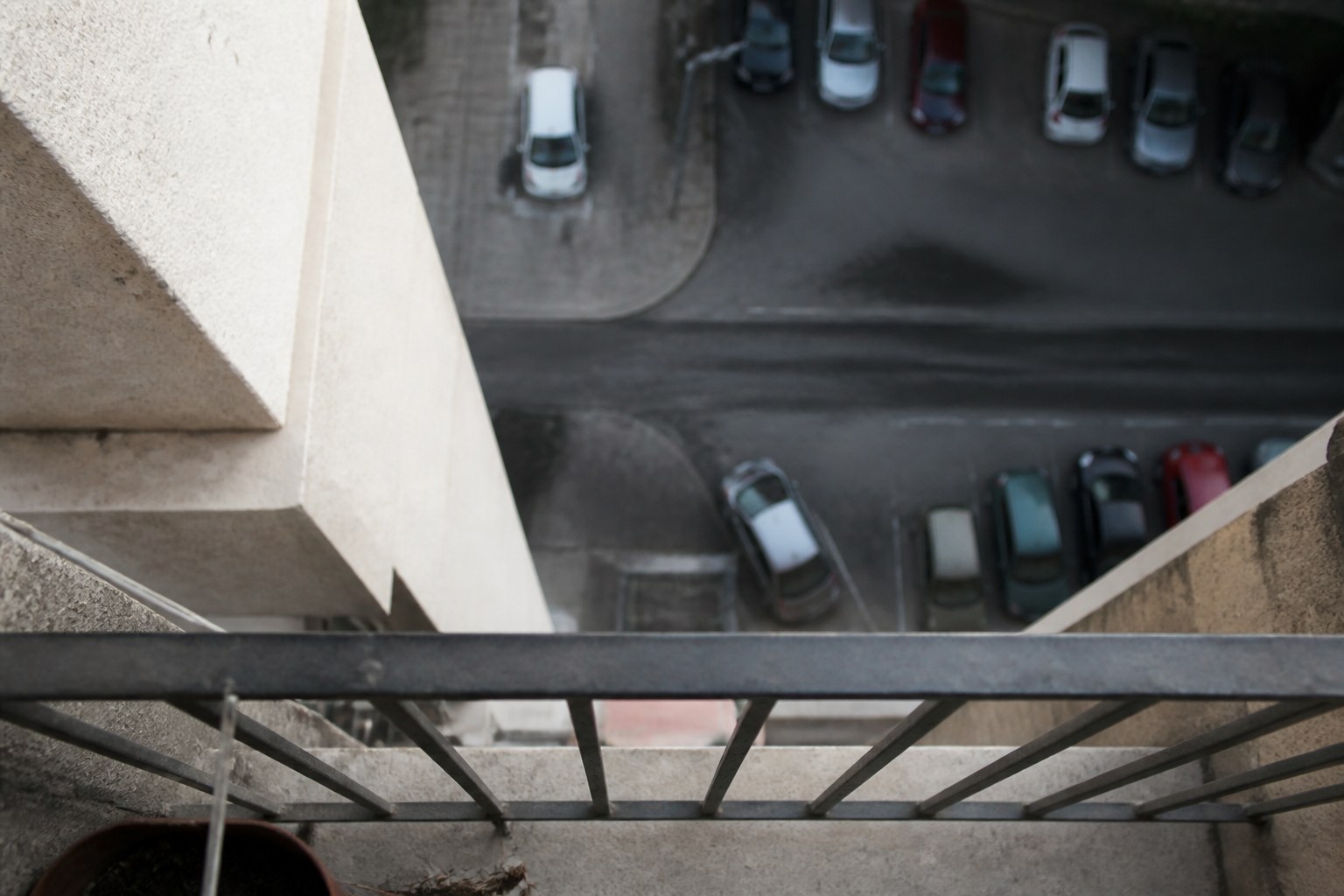 A steep downward view from a high balcony onto a street far below, the rail in the foreground