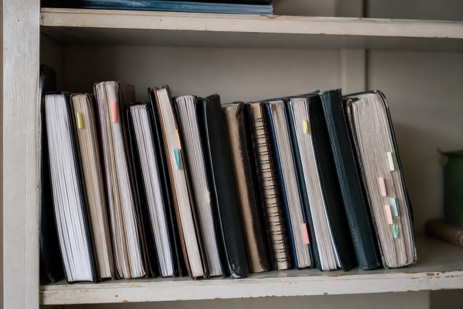 A shelf of dated notebooks with coloured sticky tabs protruding from several