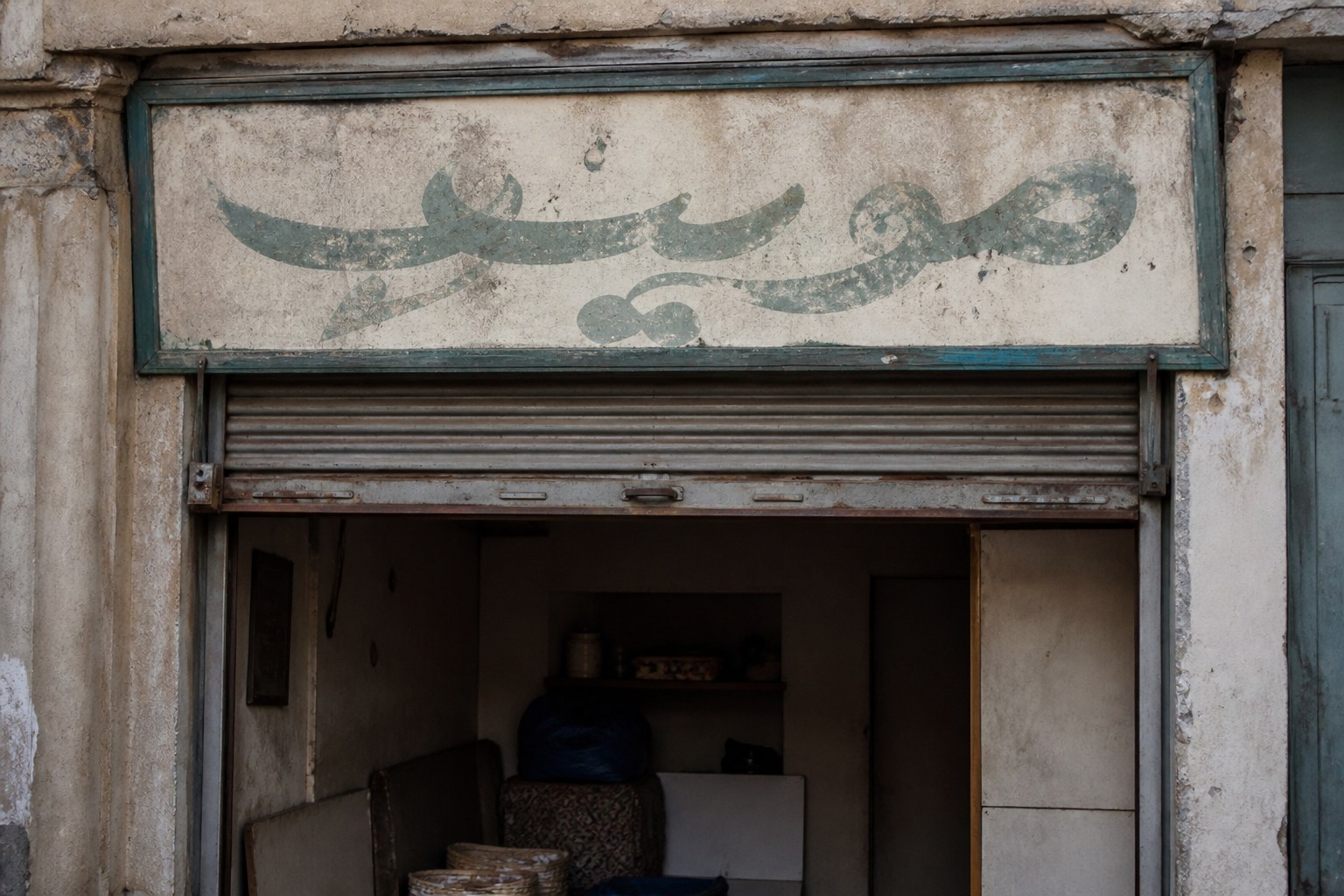 A hand-painted shop sign above a doorway carrying a single word in Arabic script
