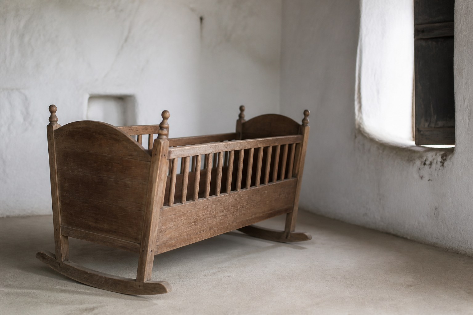 A plain wooden cradle standing empty in a quiet whitewashed room