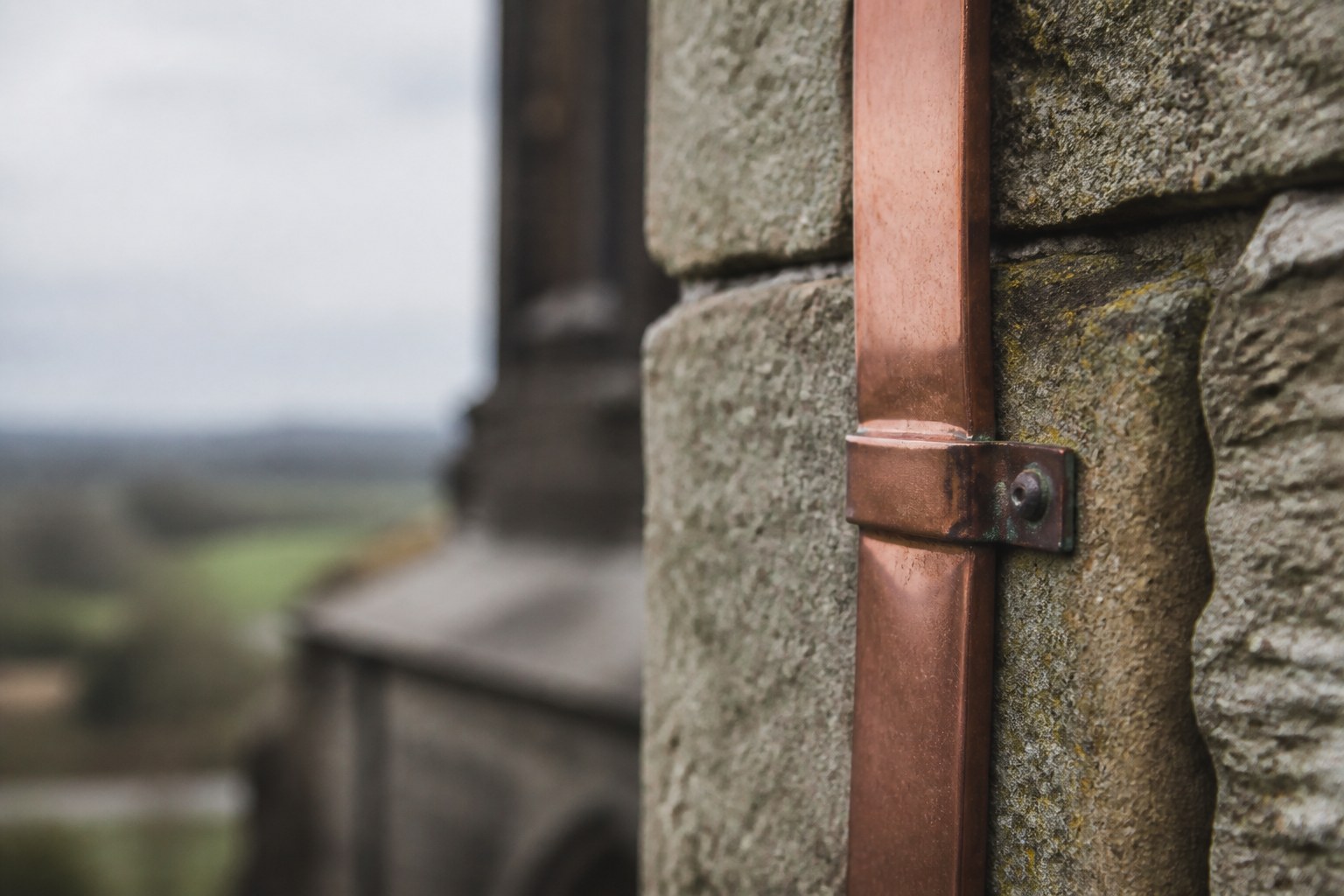 A copper lightning conductor strap running down the outside face of an old stone wall