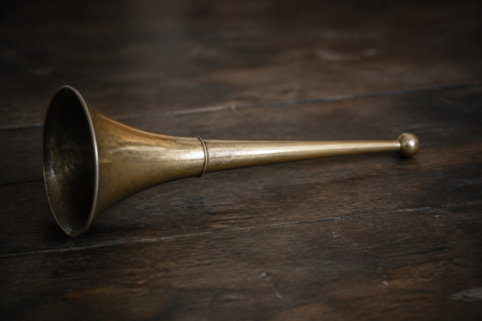 A brass ear trumpet lying on a bare wooden table in dim light