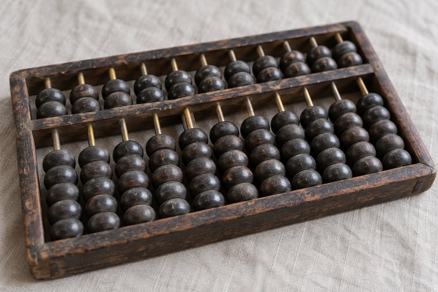 A worn wooden abacus with dark beads on brass rods, photographed close on a plain cloth