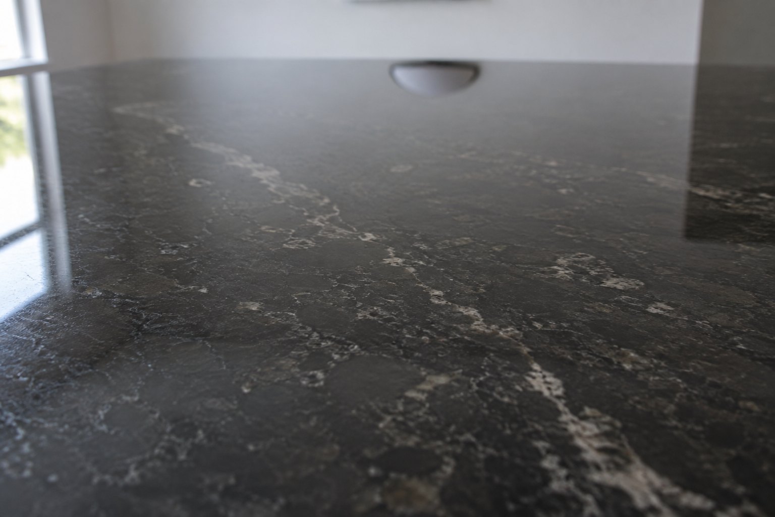 A polished slab of dark stone lying flat, returning a dim and slightly distorted reflection of a plain ceiling above it