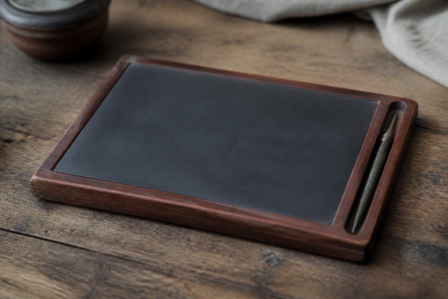 A blank wax writing tablet in a wooden frame with a bronze stylus resting alongside