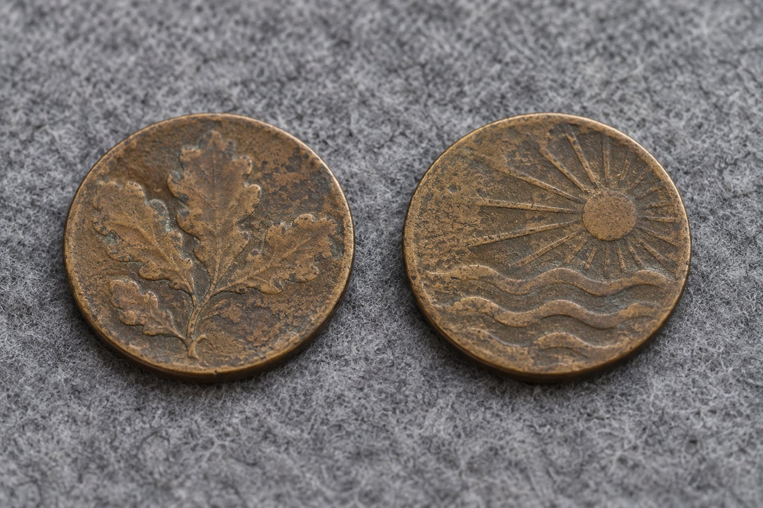 Two worn bronze coins of the same diameter lying side by side on grey felt, their designs clearly different from one another