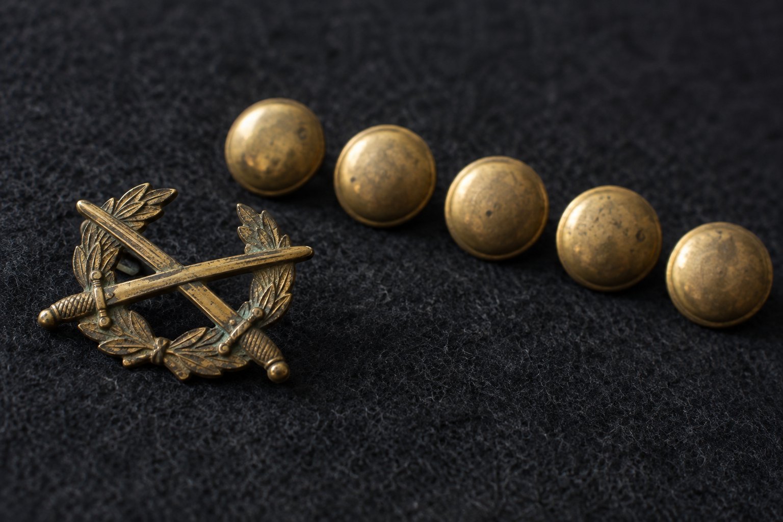 A single tarnished brass officer's insignia lying apart from a row of identical plain buttons on dark felt