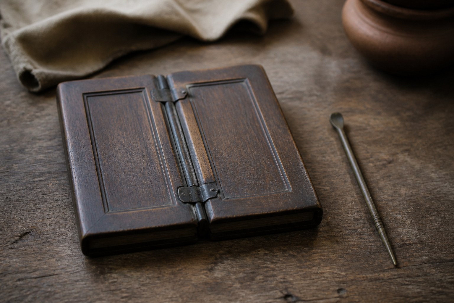 A closed pair of wooden folding wax tablets beside a bronze stylus