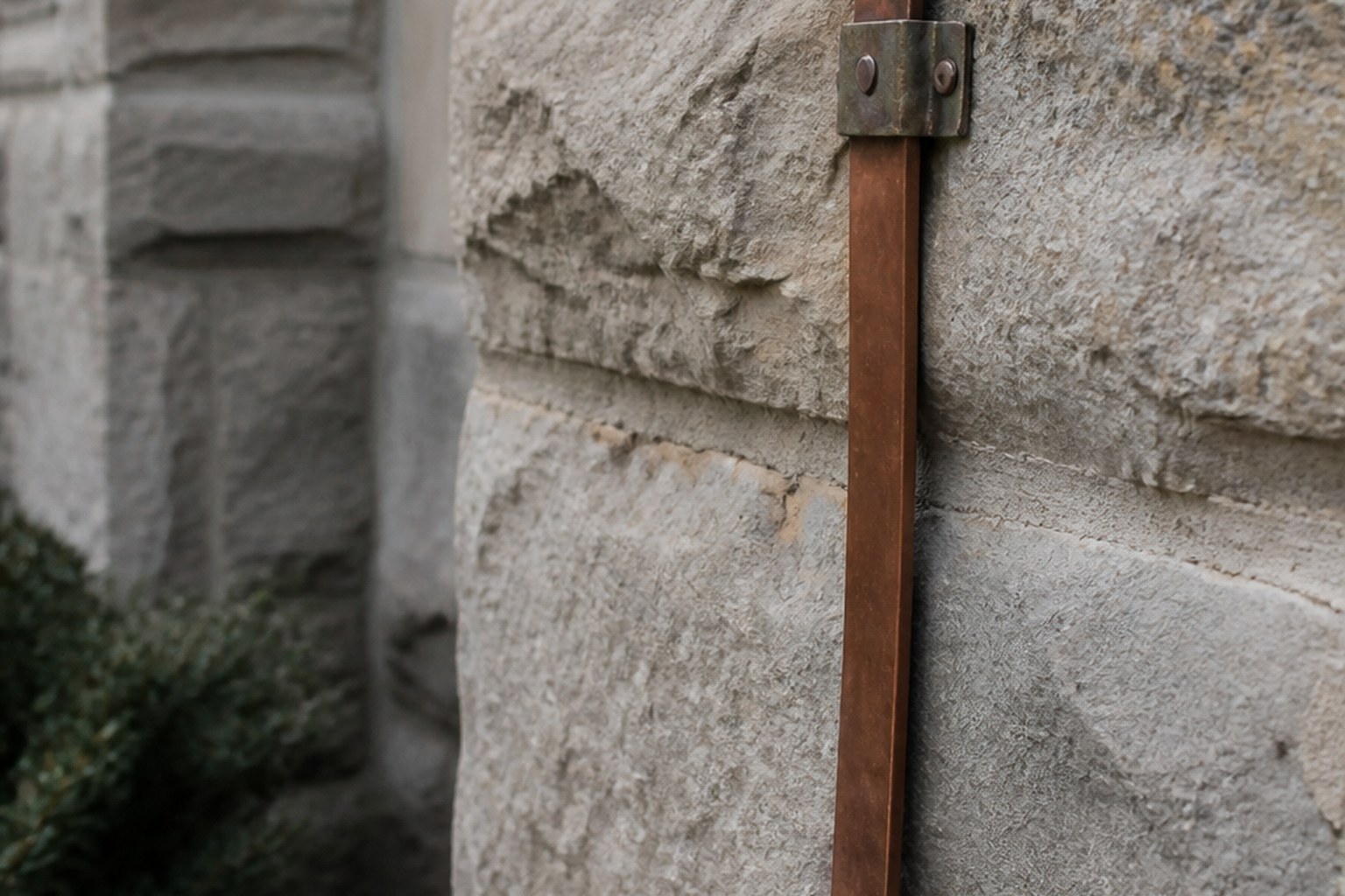 A copper lightning conductor strap running down a stone wall