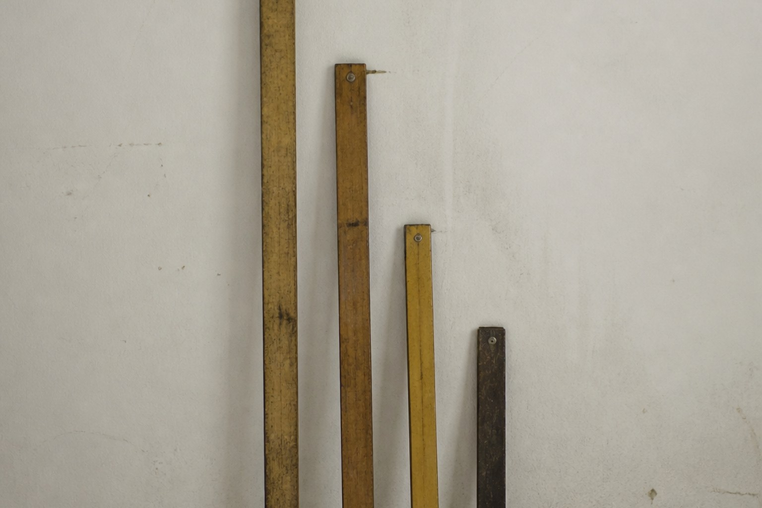 Four measuring sticks of different lengths standing against a plain wall