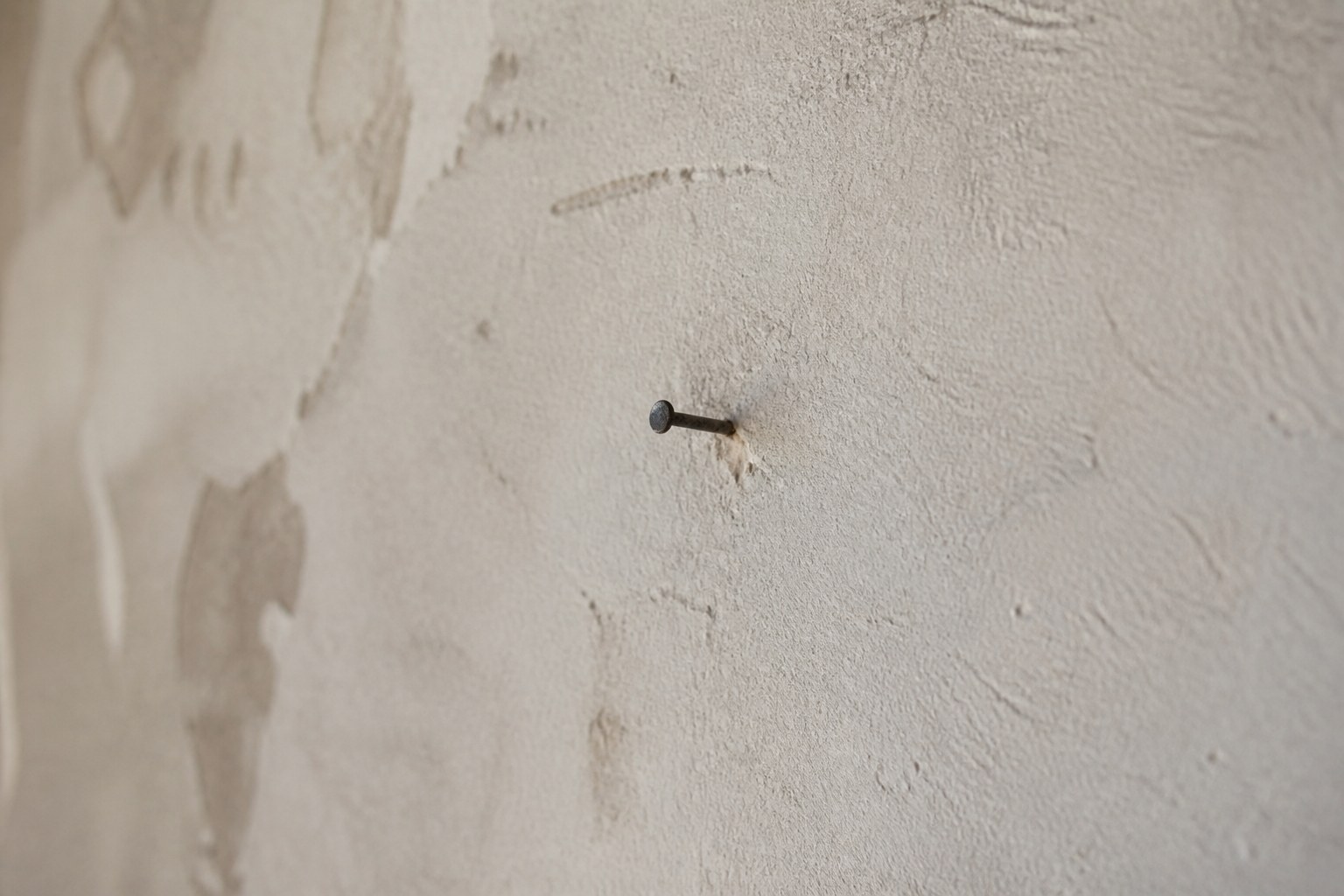A single nail in a bare plastered wall with nothing hanging on it