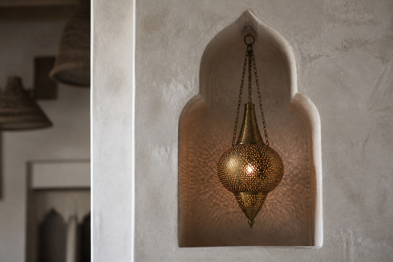 A plastered wall niche holding a hanging pierced brass lamp, warm light showing through the piercings