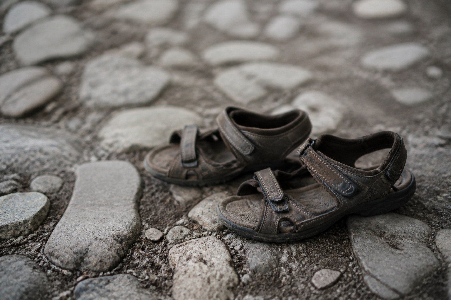 A pair of worn walking sandals set down on an old cobbled road