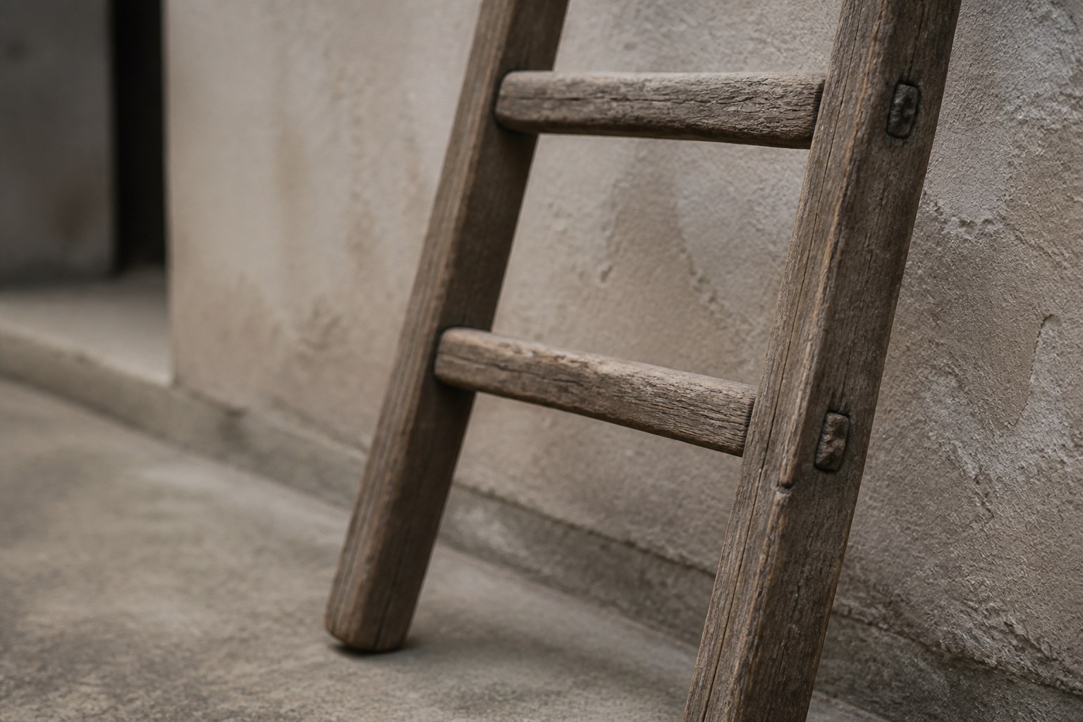 The three lowest rungs of a wooden ladder leaning against a rendered wall