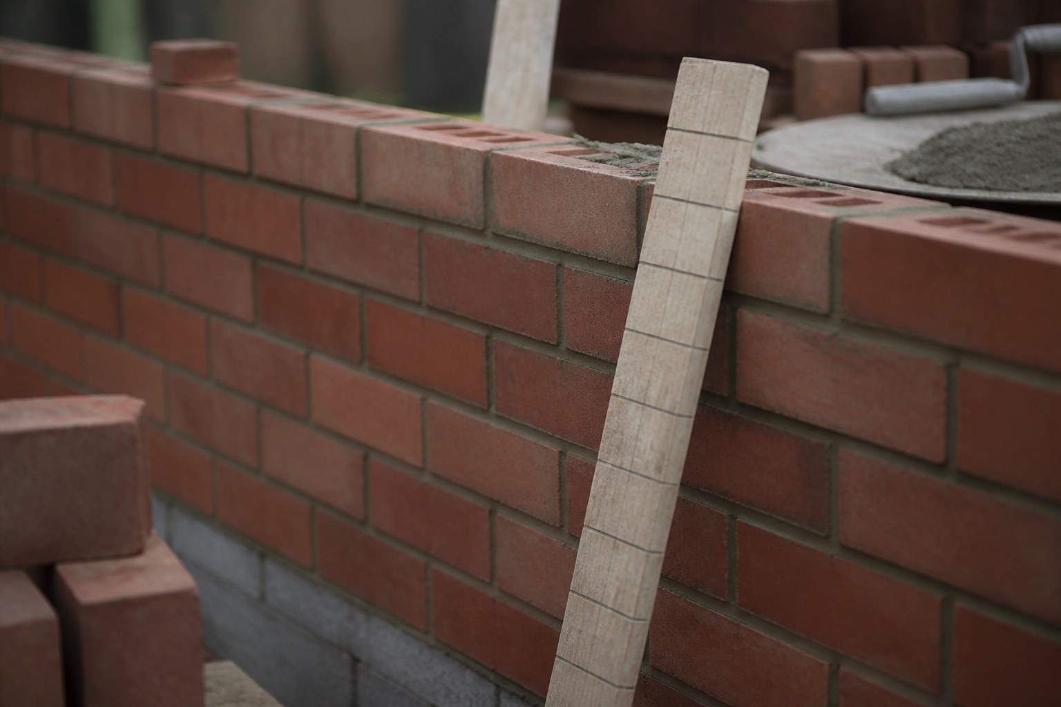 A mason's story pole marked off in even divisions leaning against fresh brickwork