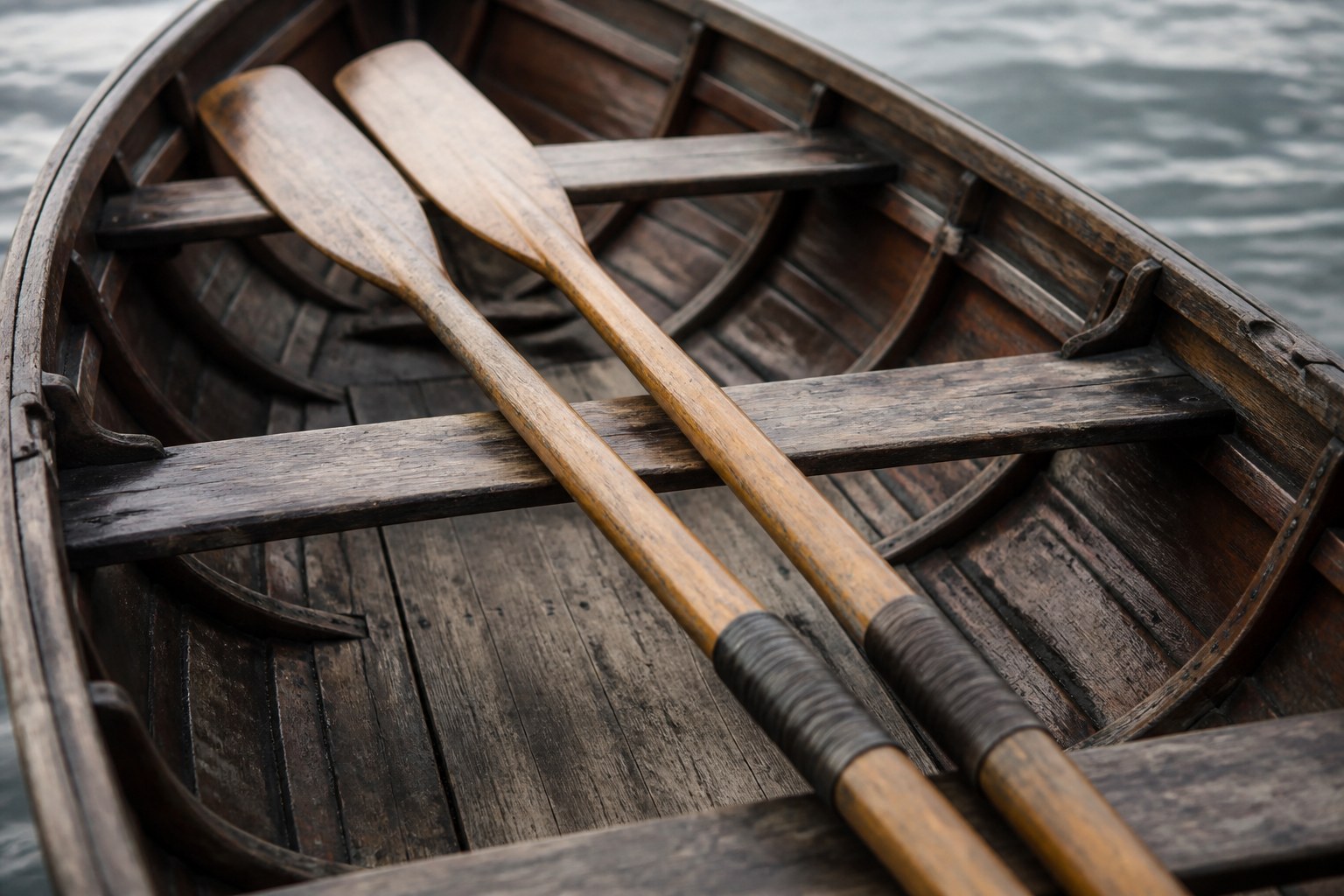 A pair of matched oars laid together across the thwarts of a wooden rowing boat