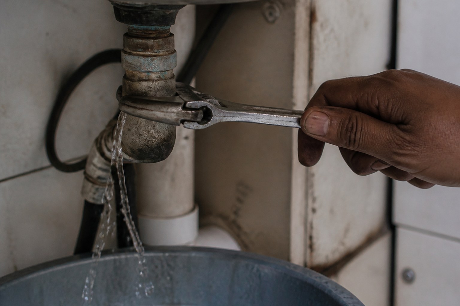 A spanner on a tap fitting under a sink with water running into a bucket