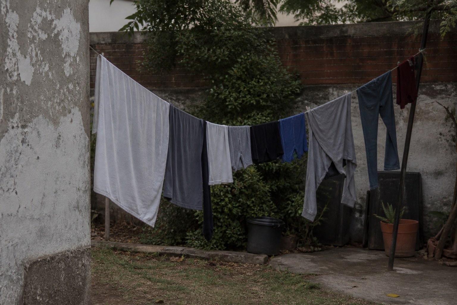 A washing line strung across a small back yard, loaded and sagging in flat daylight