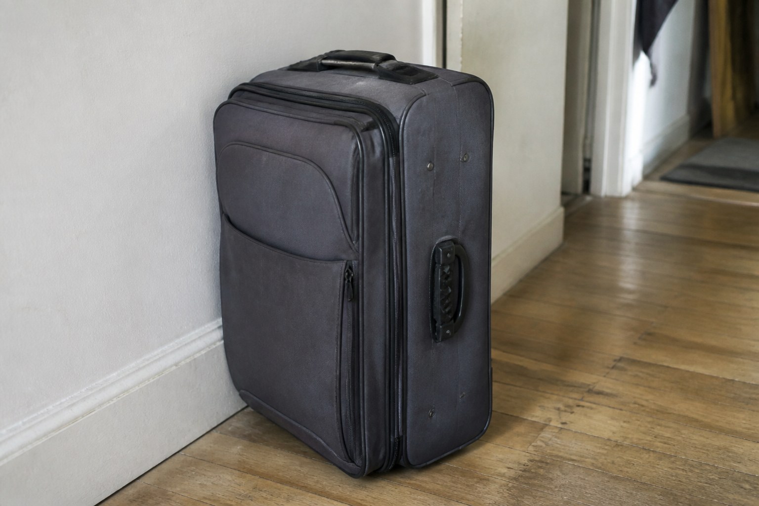 A packed suitcase standing closed in a bare hallway
