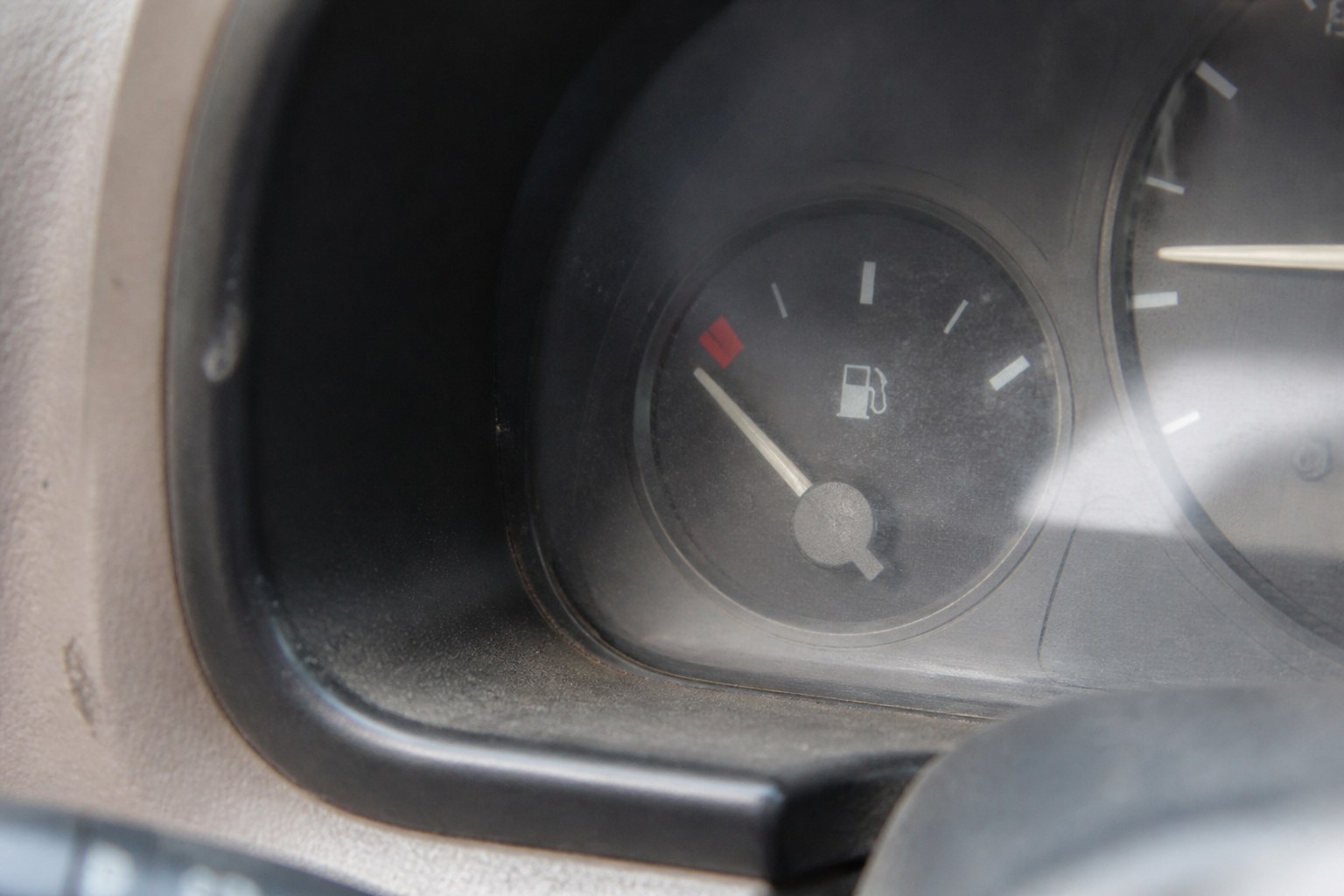 A fuel gauge needle resting on empty on a worn dashboard