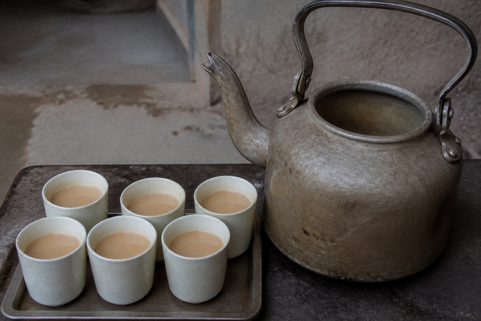 A large teapot beside a row of full cups, the pot visibly drained