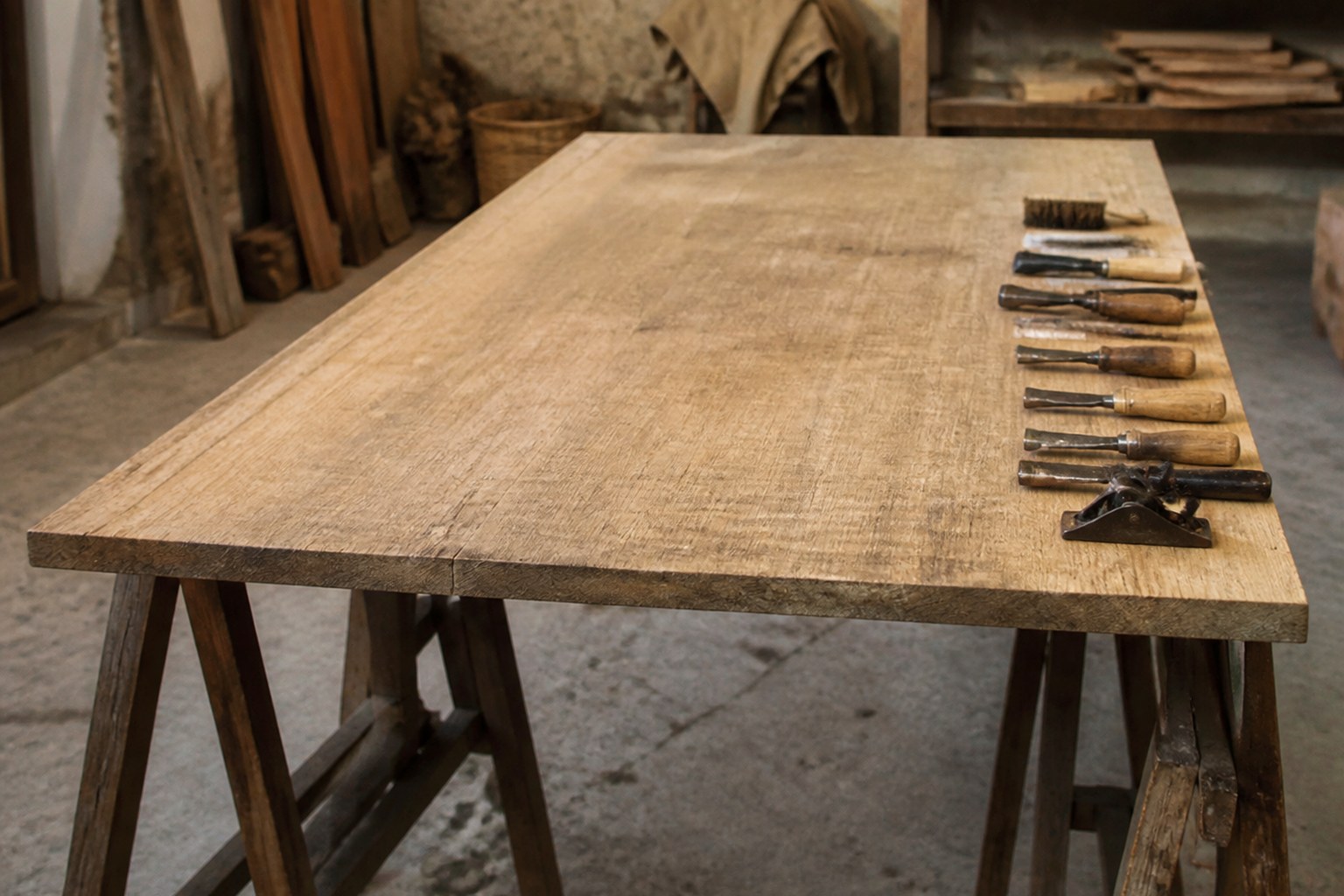 A wide board resting on two trestles in a workshop with tools laid along one edge