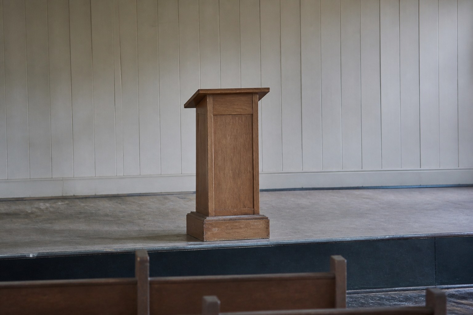 A plain wooden lectern standing alone on a low stage in an empty hall