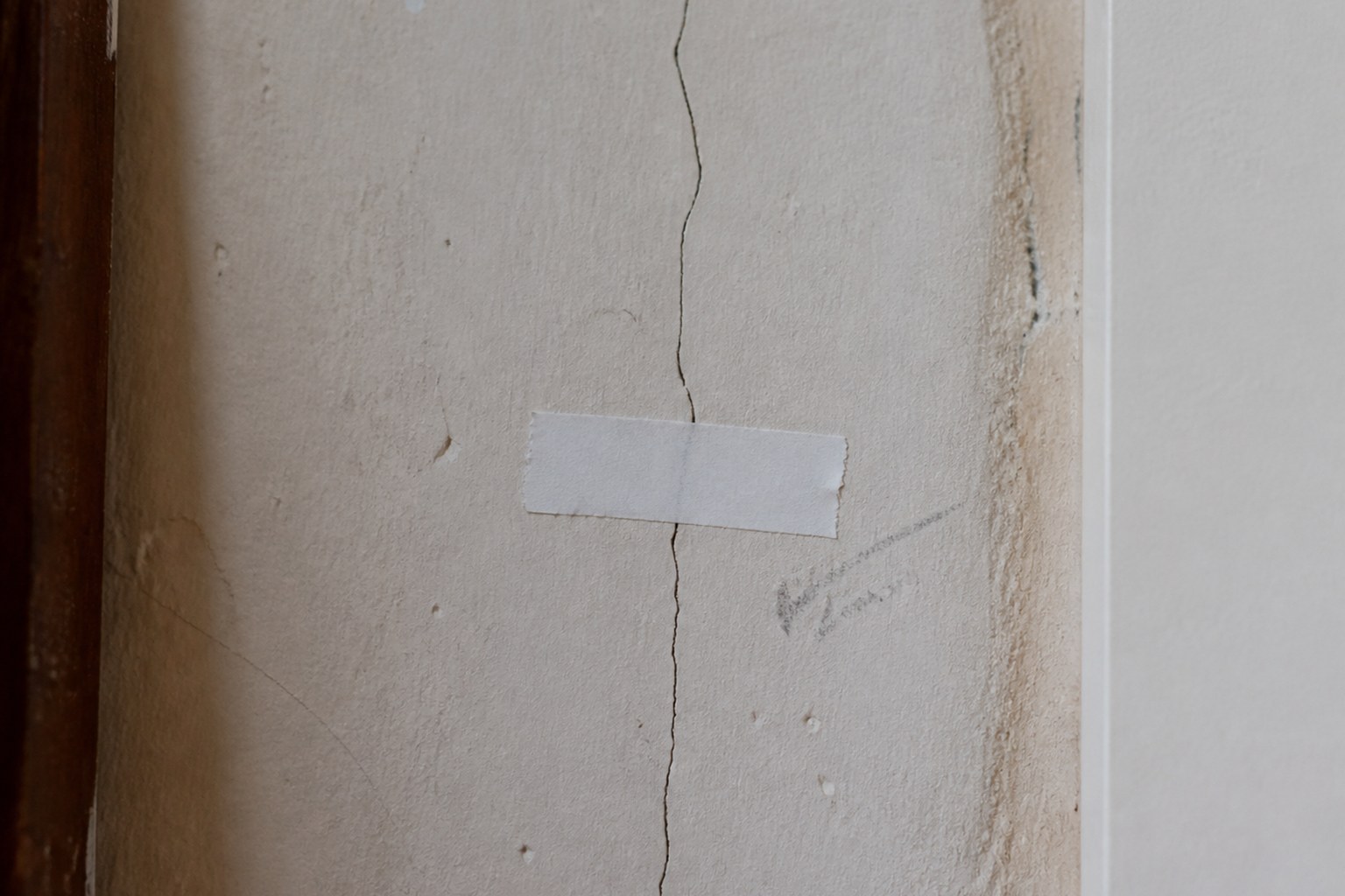 A hairline crack in plaster with a paper tell-tale glued across it