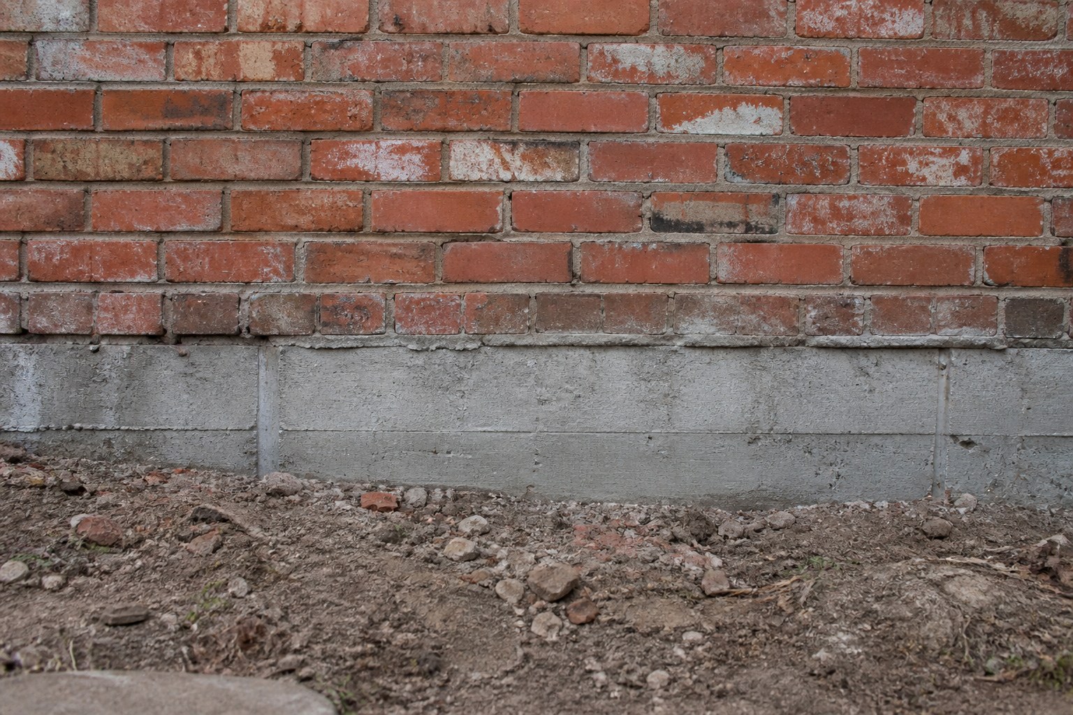 An old brick wall with a newer concrete underpinning course visible beneath it