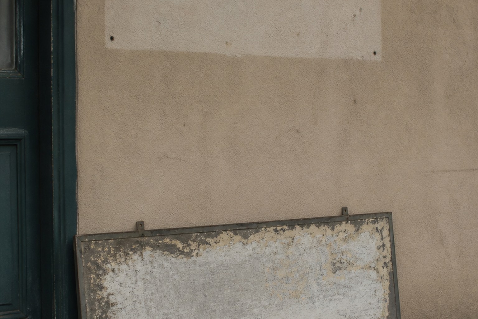 An old shop sign leaning against a wall below the brighter patch where it hung