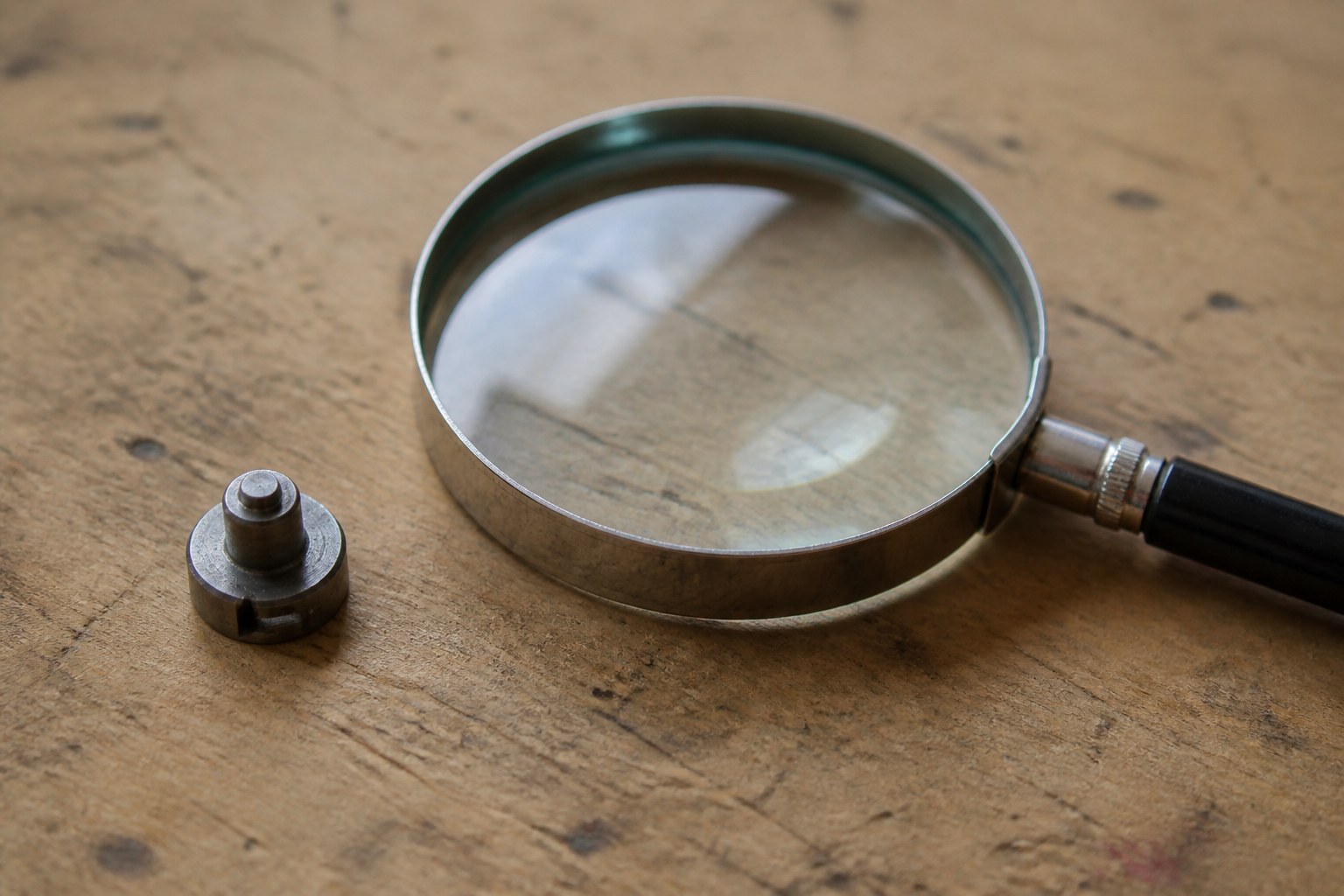 A magnifying glass on a workbench beside a single small metal component