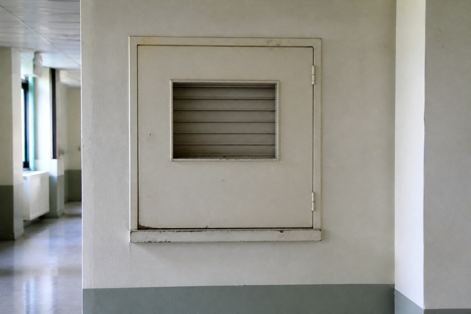 A closed service hatch with a shuttered window in a public corridor