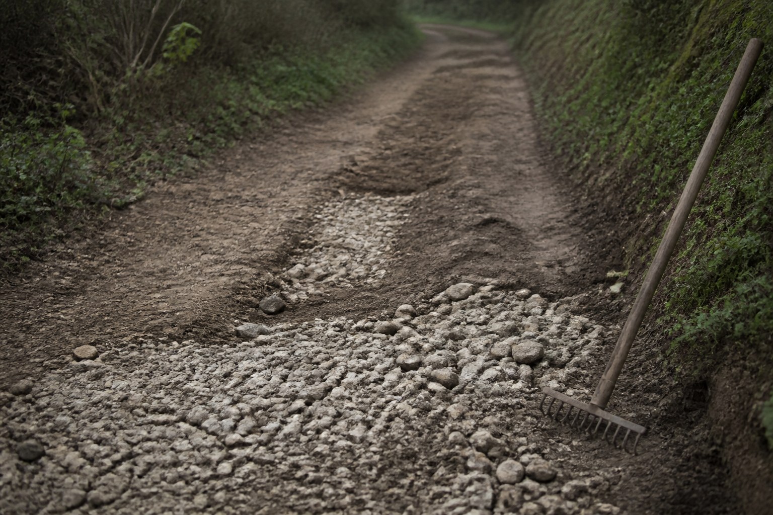 A rutted track part filled with fresh stone, a rake leaning at the edge