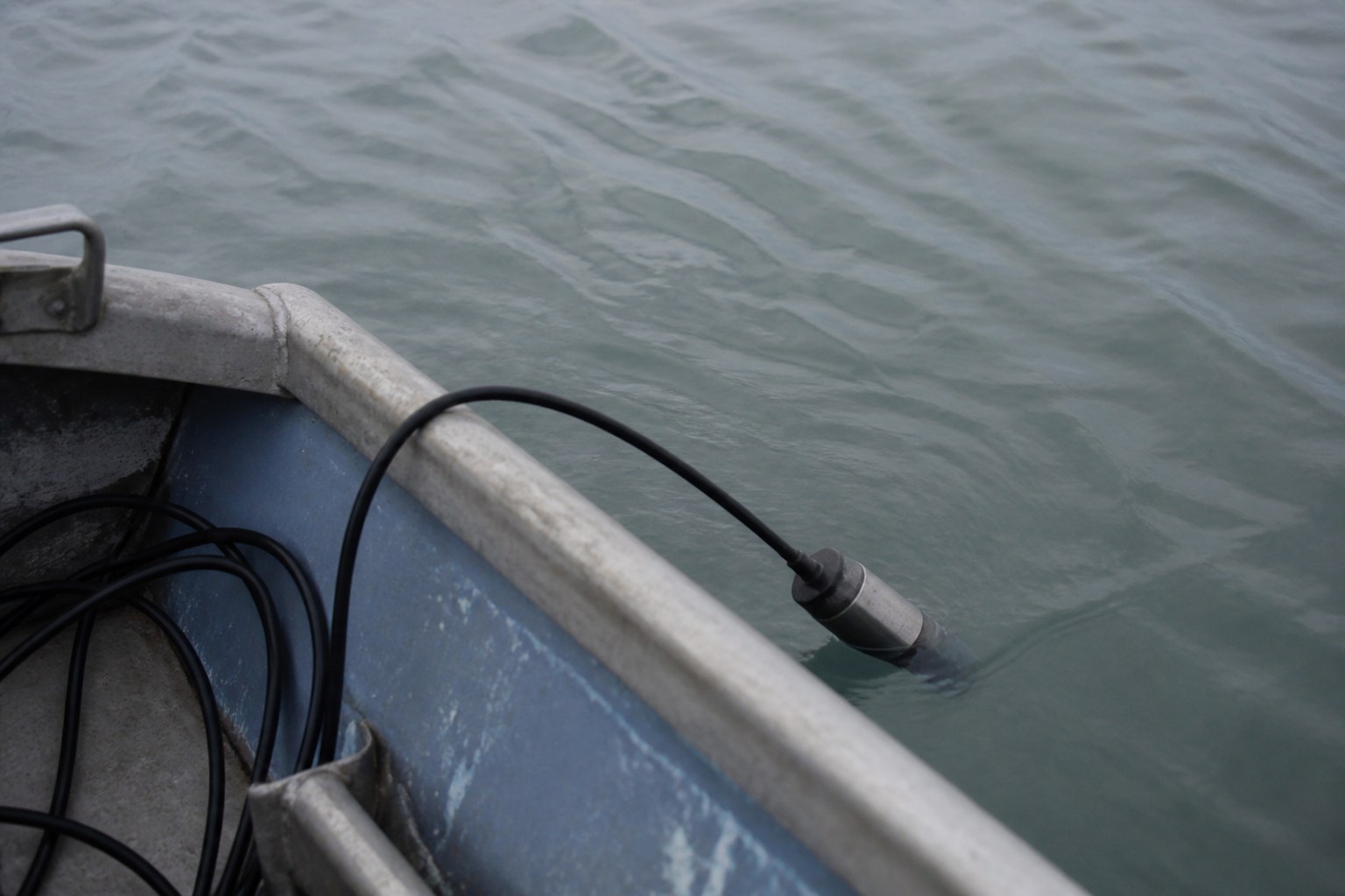 A hydrophone cable running over the gunwale of a small boat into grey water