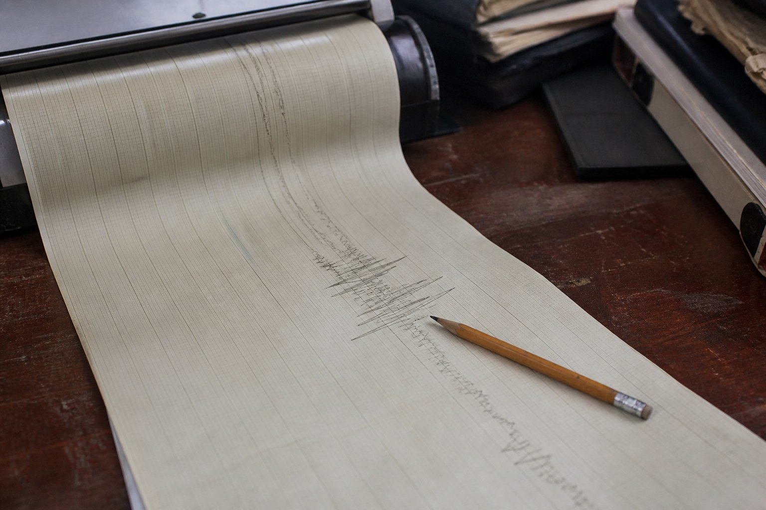 A paper chart recorder trace unrolled on a bench with a pencil on the line