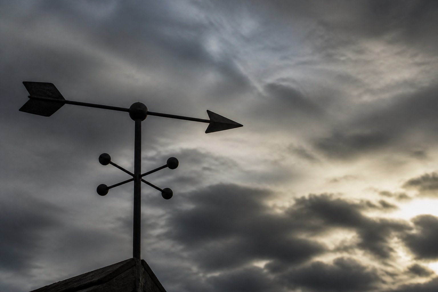 A weather vane against a moving sky, the arrow caught between directions