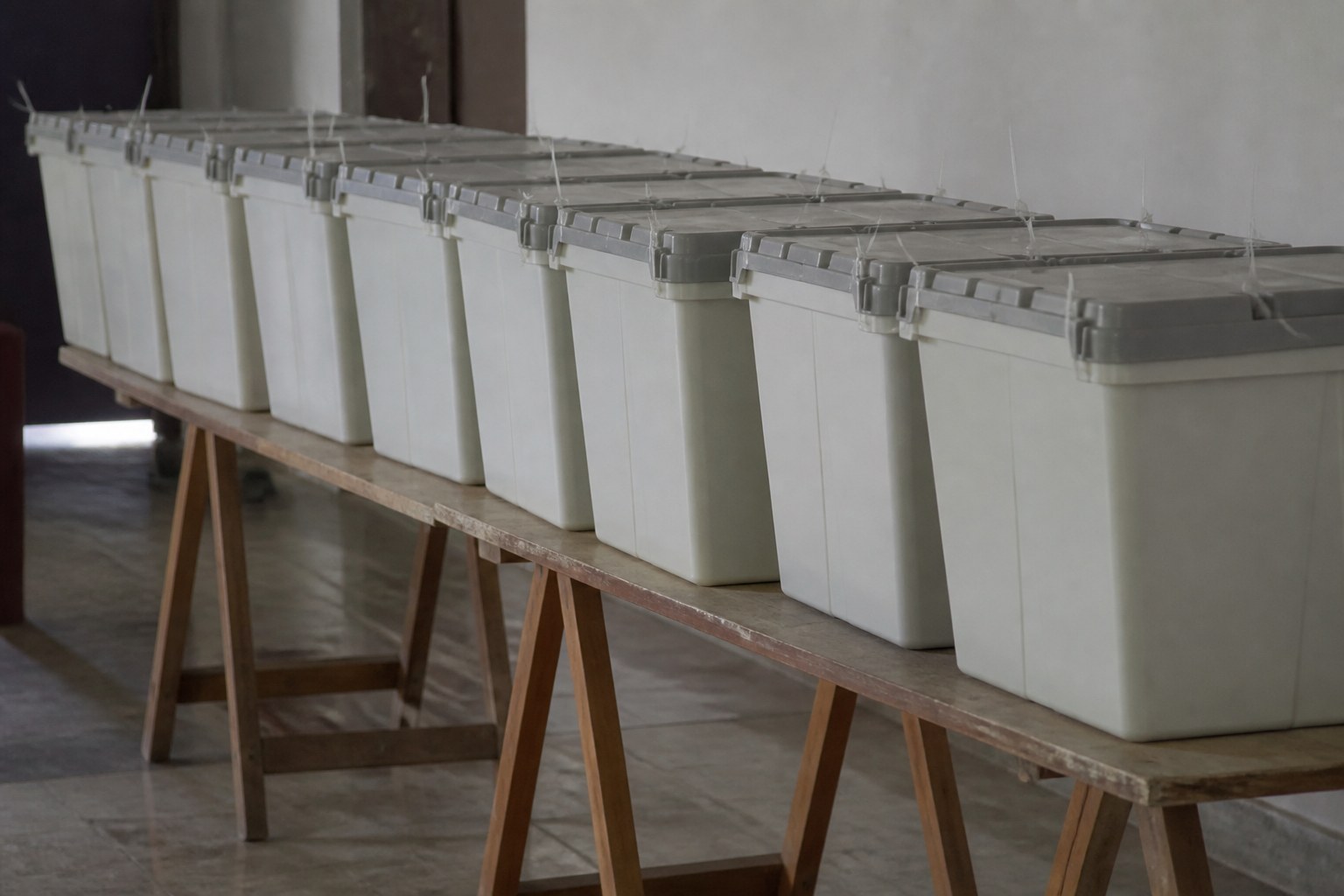 A row of sealed ballot boxes stacked on a trestle table in a plain hall