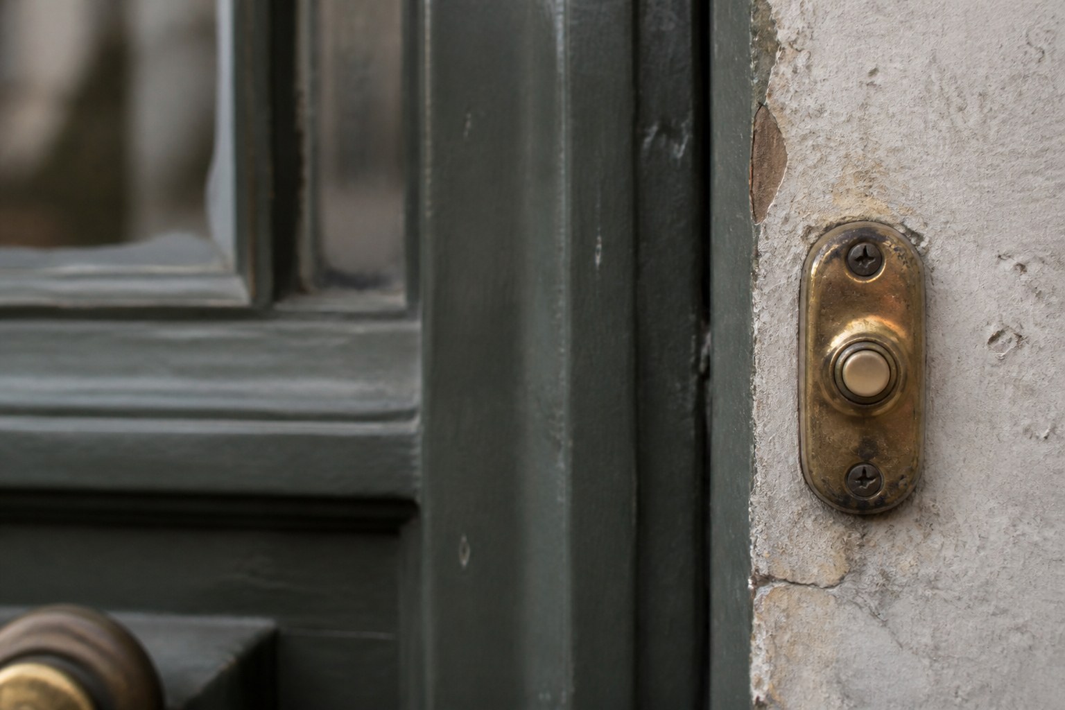 A doorbell push worn smooth beside a painted front door