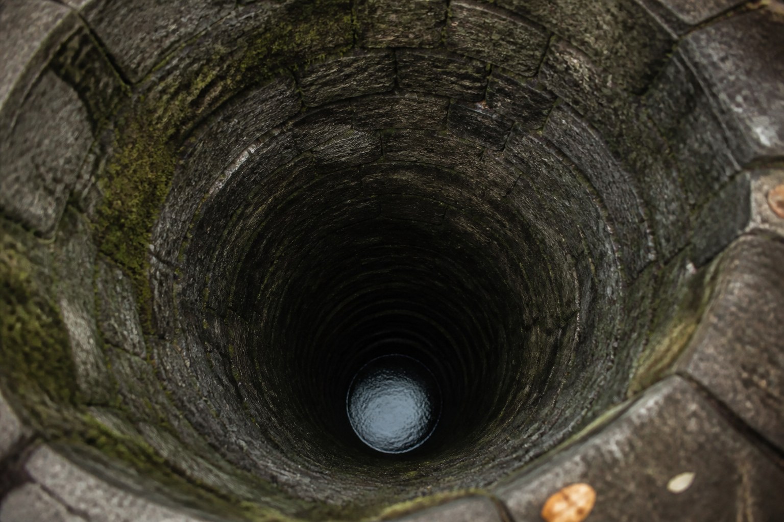 Looking straight down an old stone well shaft to a small distant disc of water