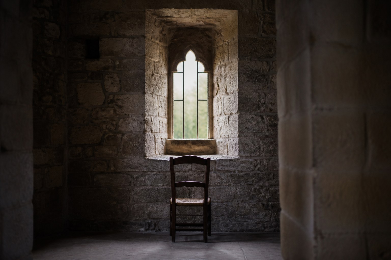 A narrow reading window in a thick stone wall with a single chair beneath it