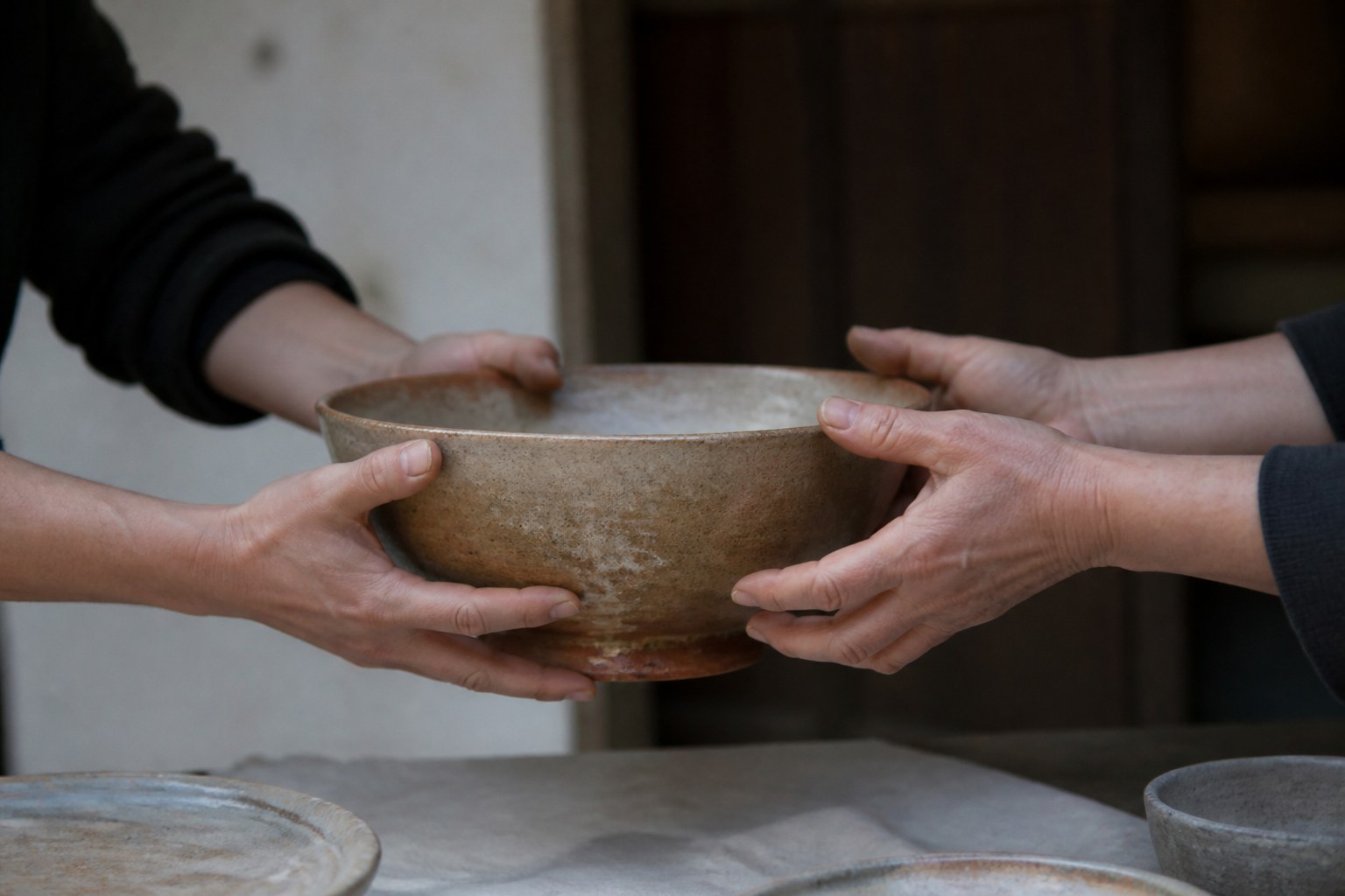 Two pairs of hands passing a heavy earthenware bowl between them