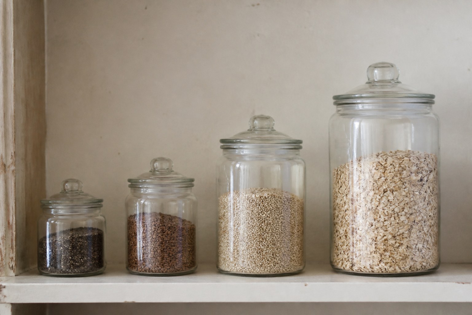 Four storage jars of increasing size in a row on a shelf