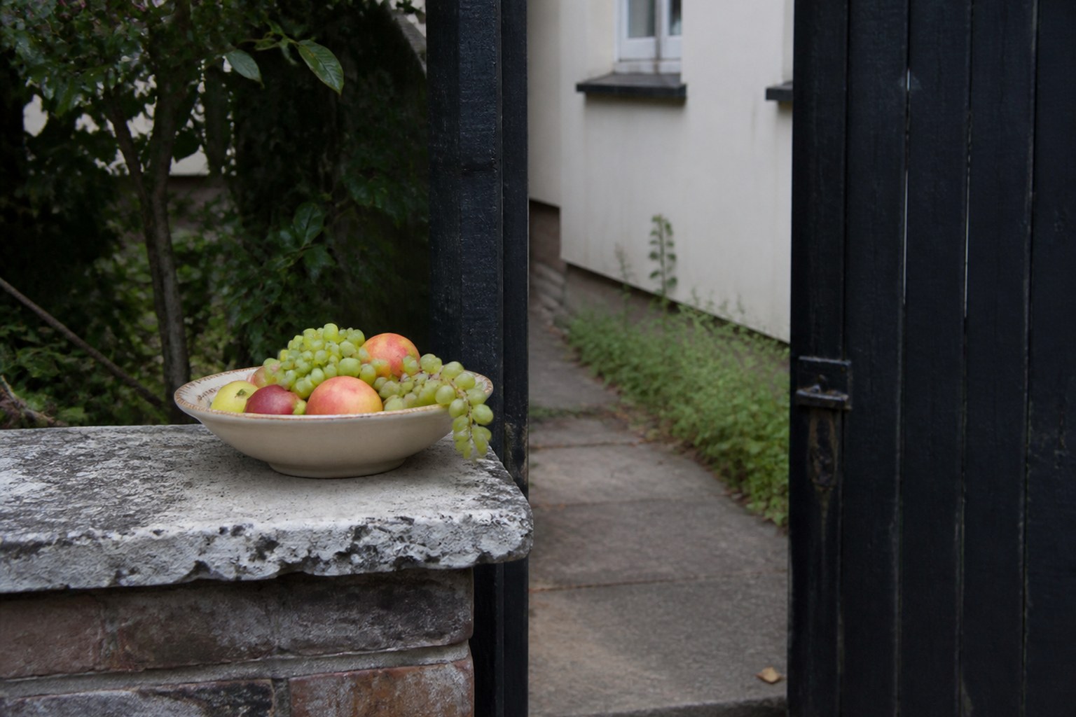 A bowl of fruit left out on a low garden wall beside an open gate
